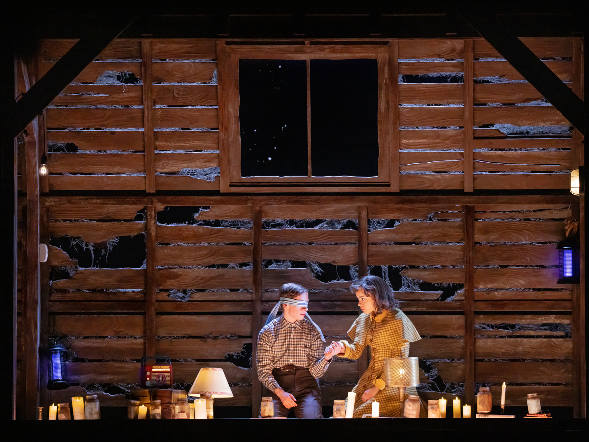 Henry Creel and Patty Newby sit in an attic surrounded by candles in Stranger Things: The First Shadow on Broadway